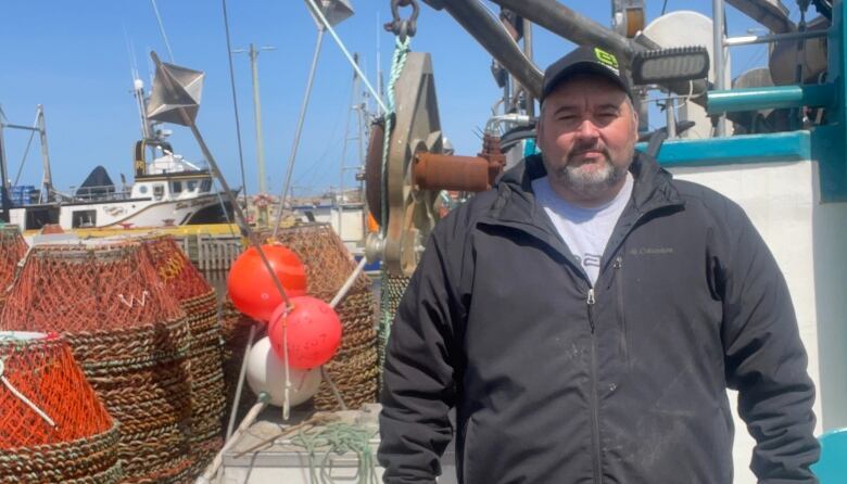 A man wearing a windbreaker stands in front of a fishing boat.