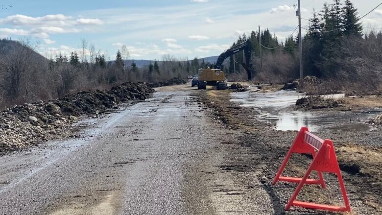 Construction machinery is seen working on a road with water on the side of the roadway.