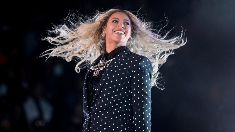 A woman wearing a polka dotted suit smiles and looks into the distance.