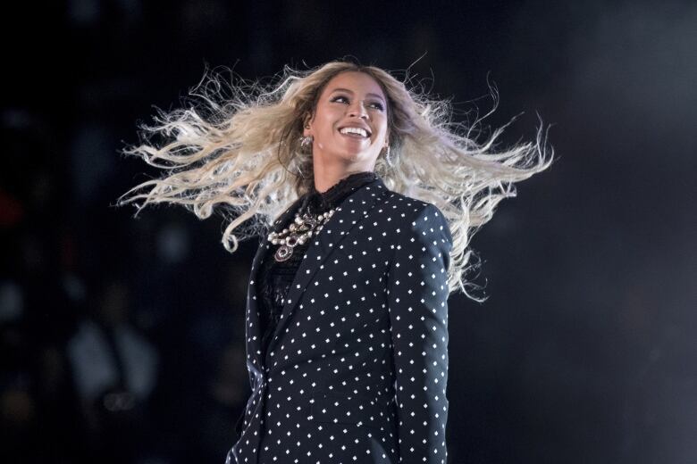 A woman wearing a polka dotted suit smiles and looks into the distance.