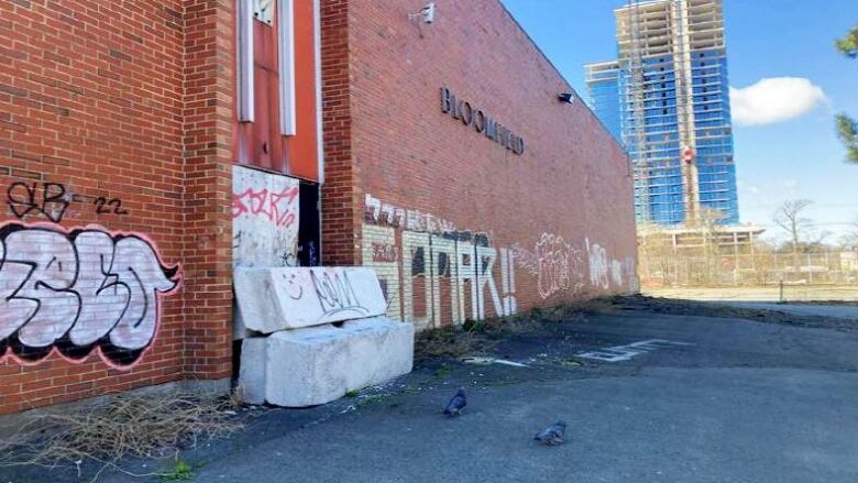 A brick school facade is tagged with graffiti, and multiple grey concrete blocks block a door opening