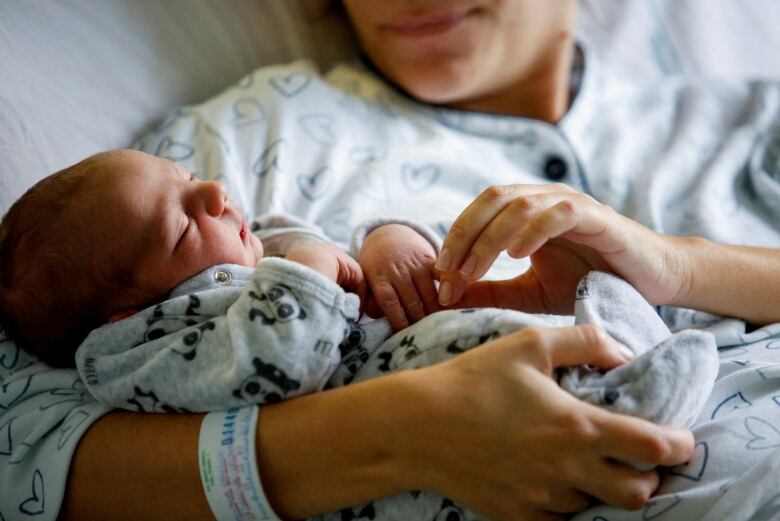 A newborn is held by a mother lying in a bed.