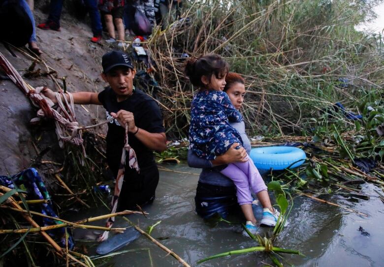 Two adults and a child prepare to walk into a body of water.