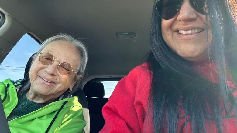 A mother and daughter sit in a car together side-by-side.