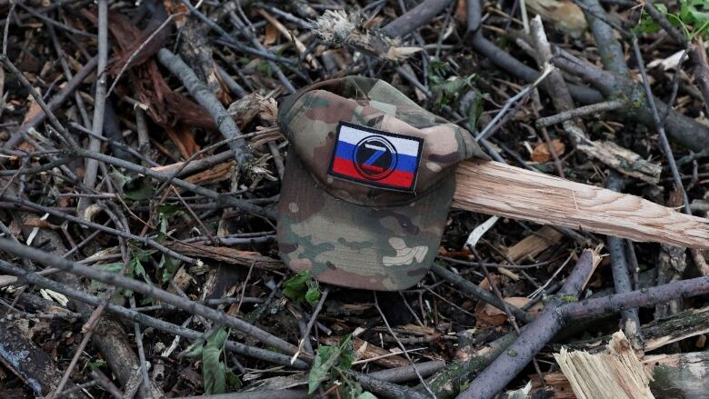 A camoflauge-coloured cap, featuring a Z symbol on a Russian flag patch, is seen on the ground of a wooded area.