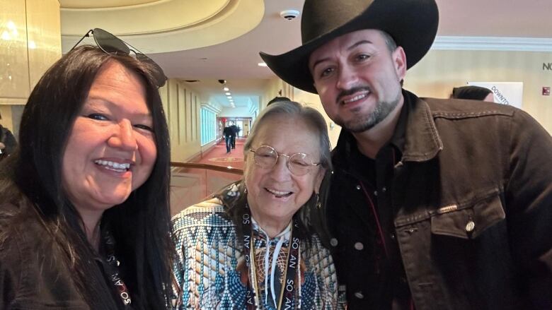 Two women and a man wearing a cowboy hat take a selfie together.