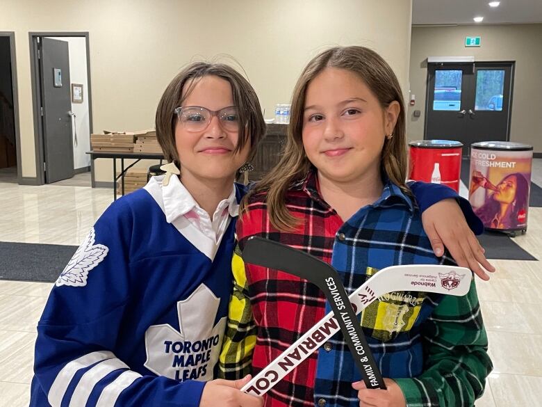 Two girls with hockey sticks smile. 