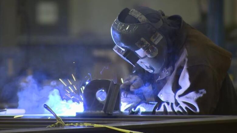 A worker wearing a mask welds metal inside a factory. 