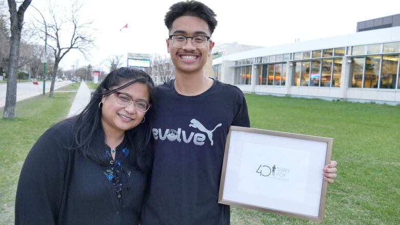 A teen boy is pictured holding an award, standing next to his mom, as both smile to the camera.