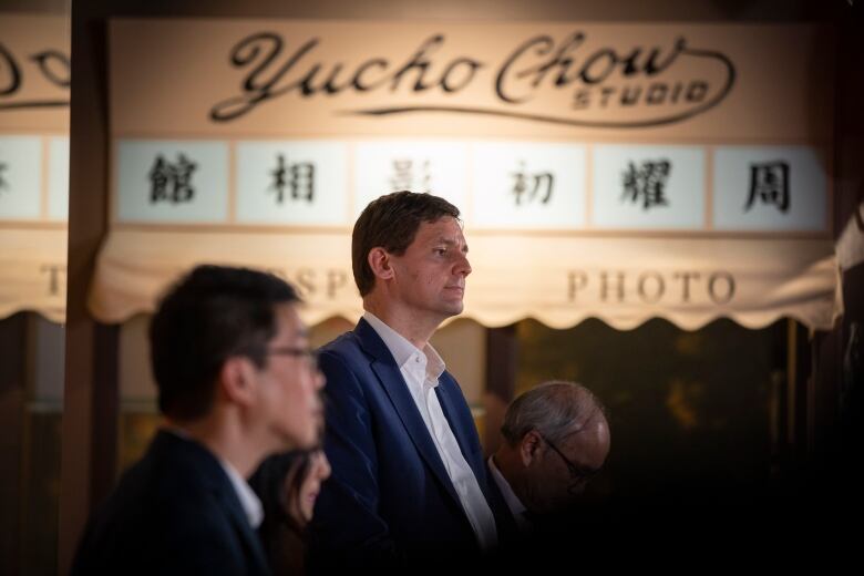 B.C. Premier David Eby stands in between two men with a Yucho Chow Studio sign in the background. 