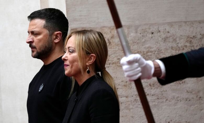 A dark-haired man and a blond woman, both wearing black, stand side by side