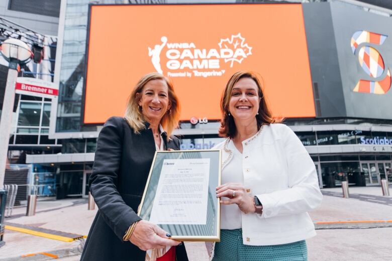 Two women holding a plaque smile for a photo.