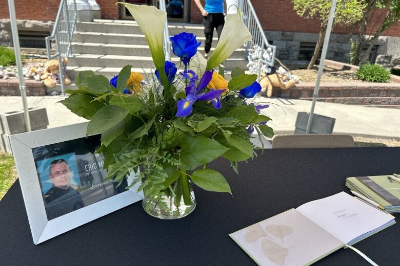 A picture frame, a vase of fllowers and books of condolences sit on a table. 