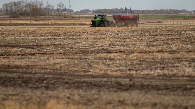 A tractor drives through a field pulling farming equipment.