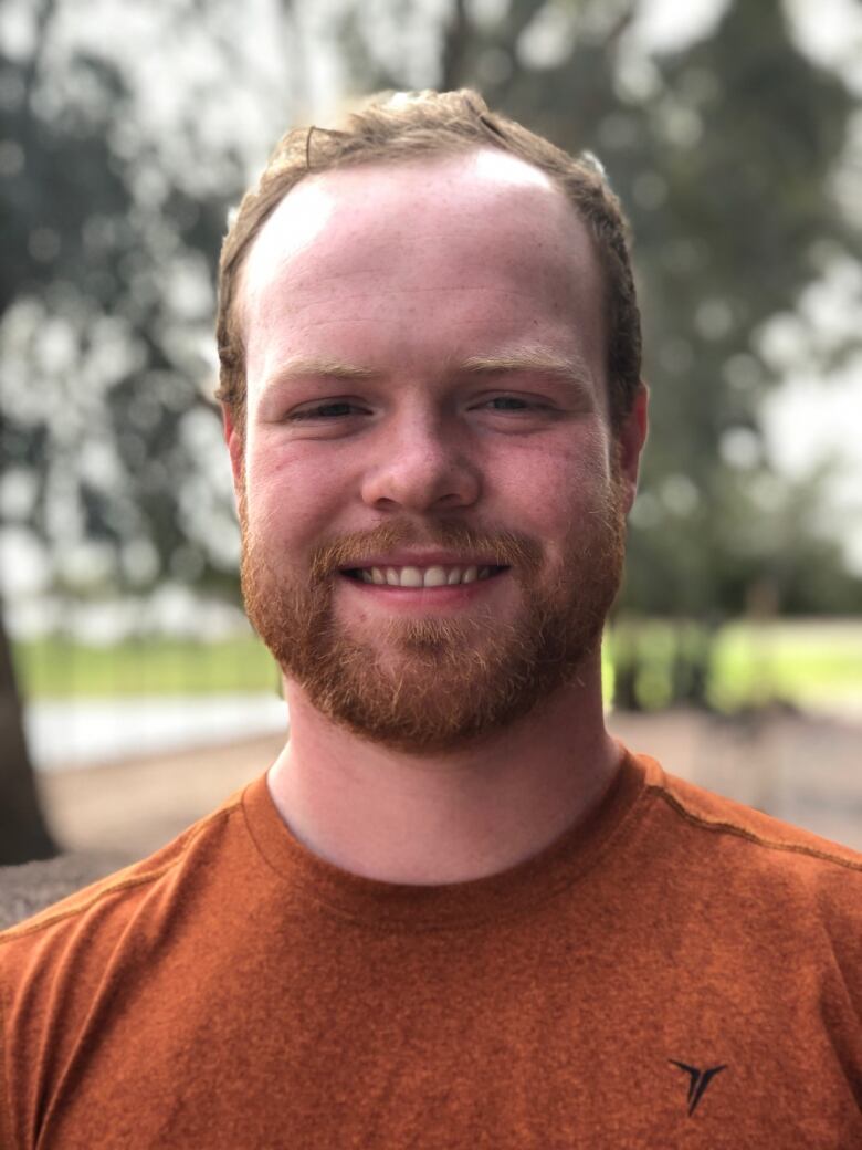 A man smiles for a photo wearing an orange shirt.