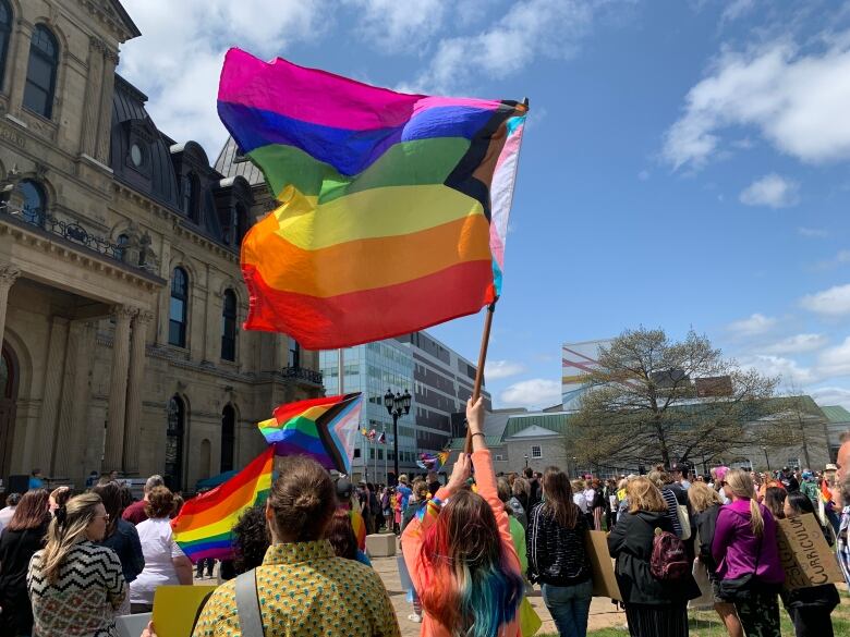 A group of people stand outside a historical building waving pride flags.