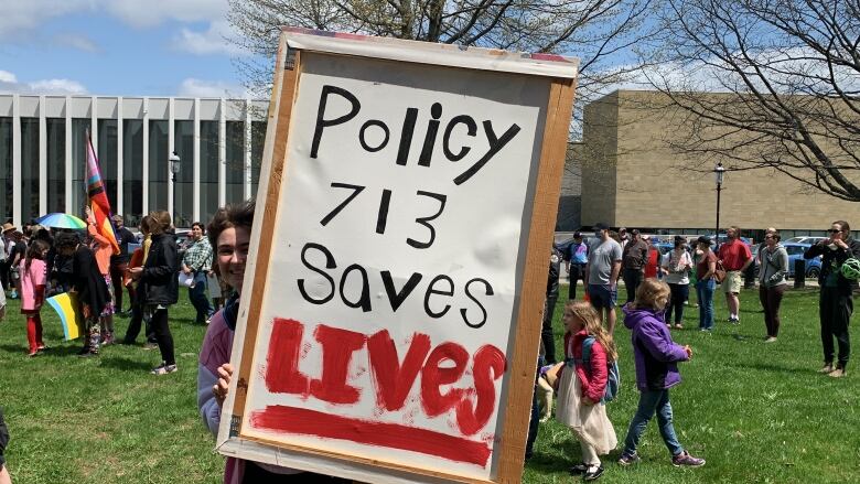 A student stands behind a homemade sign that says 