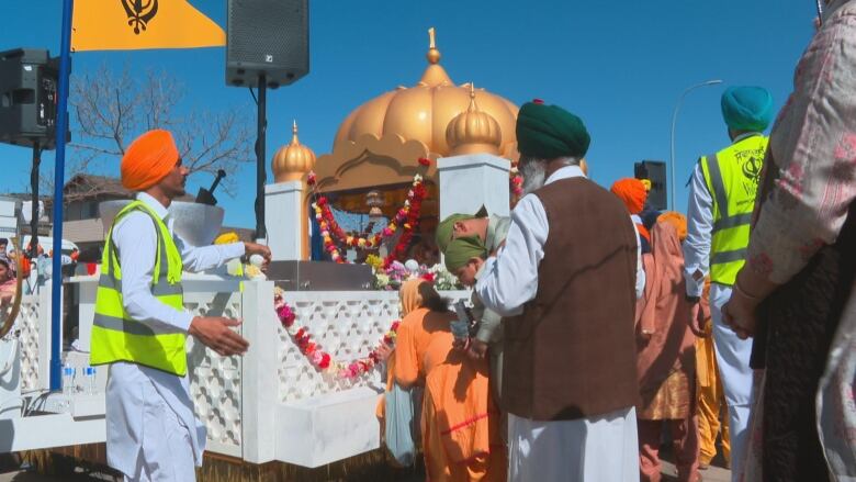 A temple is pictured in the background with several people in colourful attire standing in front.