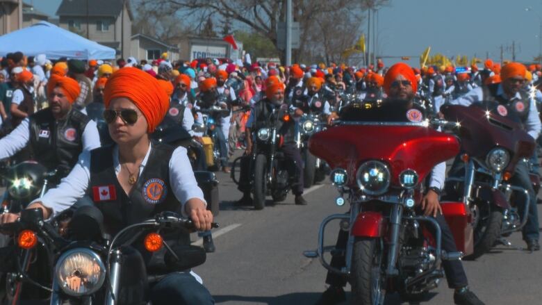 A group of people wearing orange turbans are pictured on motorbikes.