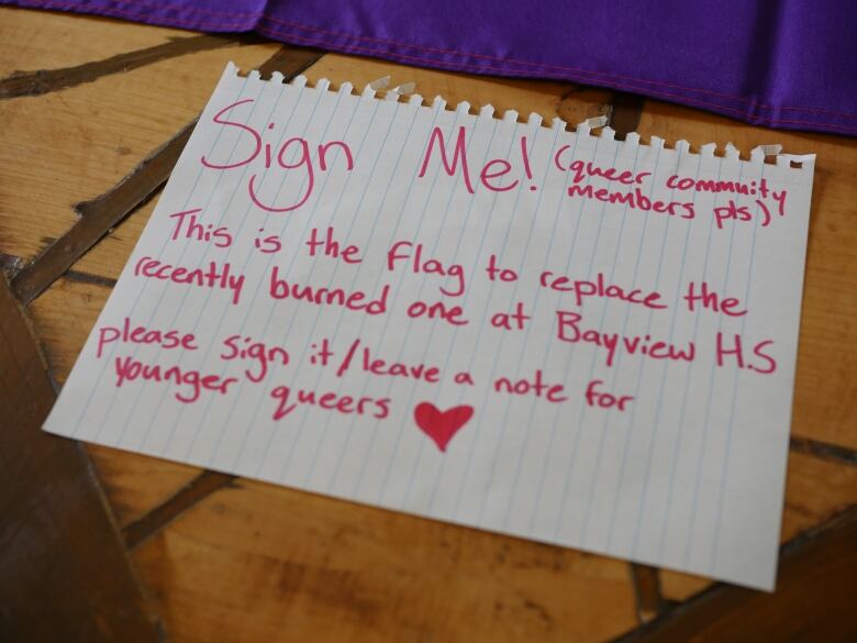 A sign reads: This is the flag to replace the recently burned one at Bay View HS. Please sign it/leave a note for younger queers