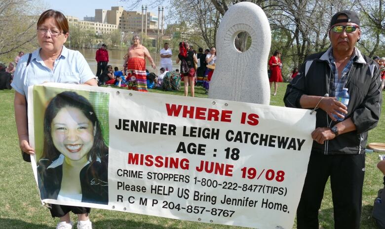 A mother and father are pictured holding up a banner with a photo and information regarding their missing daughter.