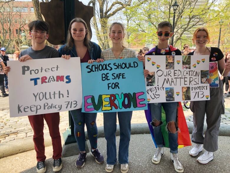 Five teenagers standing next to one another holding posters. The poster on the far left says 