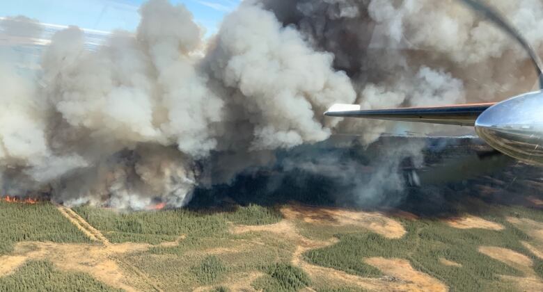 Airplane wing, smoke, flames over brown and green landscape.