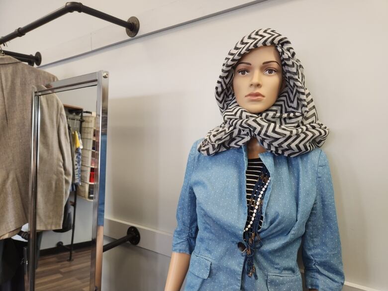 A mannequin wears a black and white striped scarf on its head and a blue jacket with white polka dots.