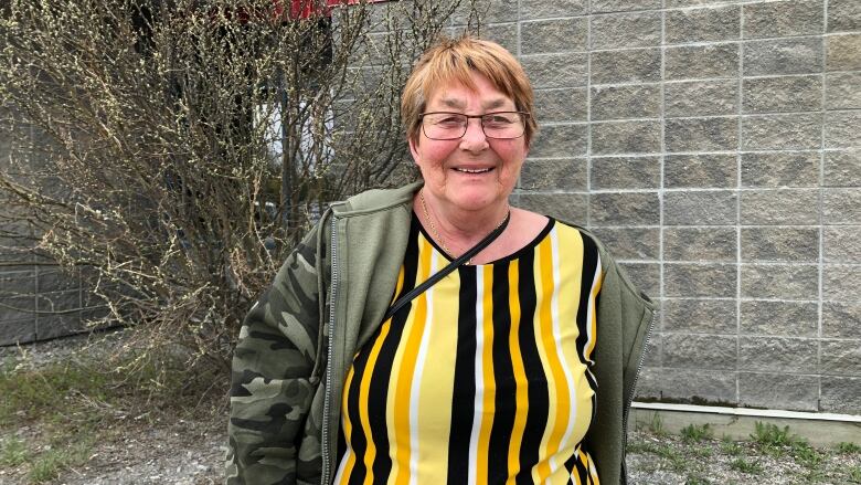 A woman wearing a yellow shirt stands outside a building. 