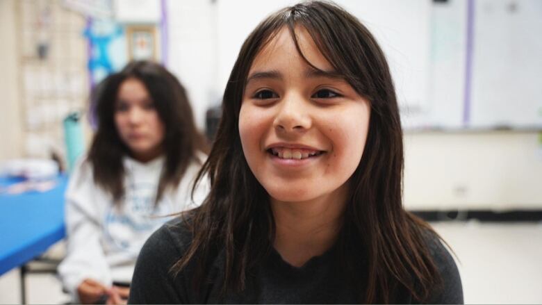 A young girl sits on a chair in a classroom. 