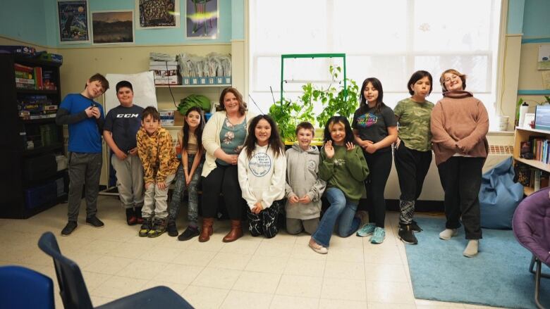 A group of students smile in front of a set of windows and some plants. 