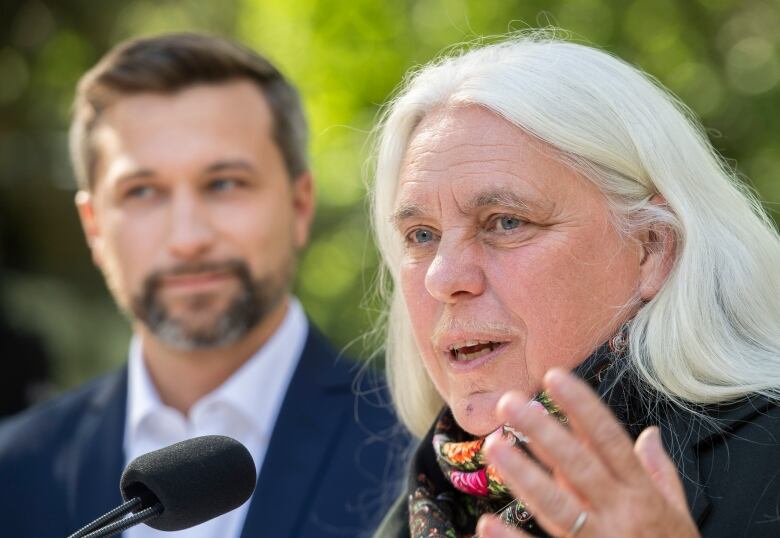 A woman speaking into a microphone next to a man. 