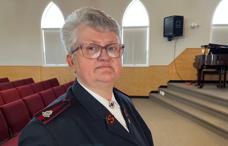 A grey-haired woman with glasses stands in a church.