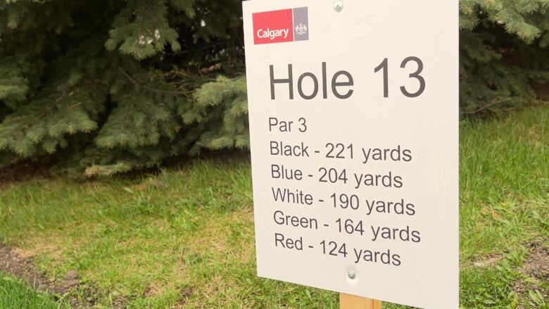 A sign on the 13th hole shows different distances to the hole from various tee boxes.