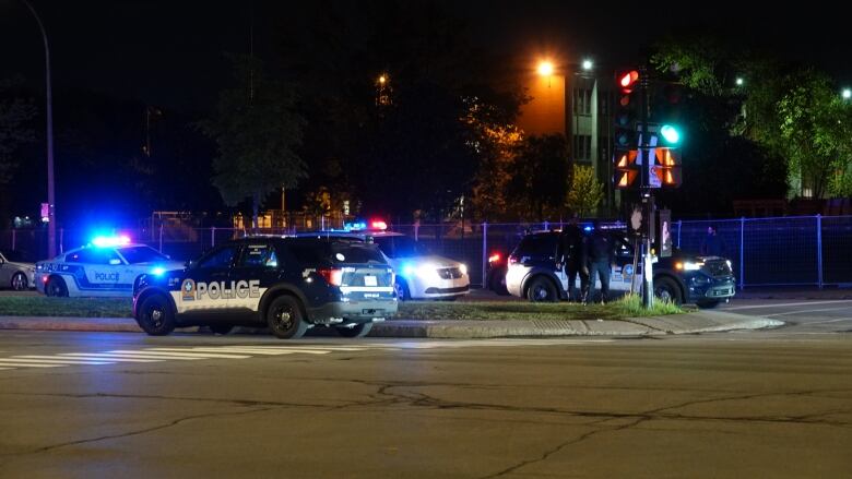 Officers stand in front of Montreal police cruisers parked at night.