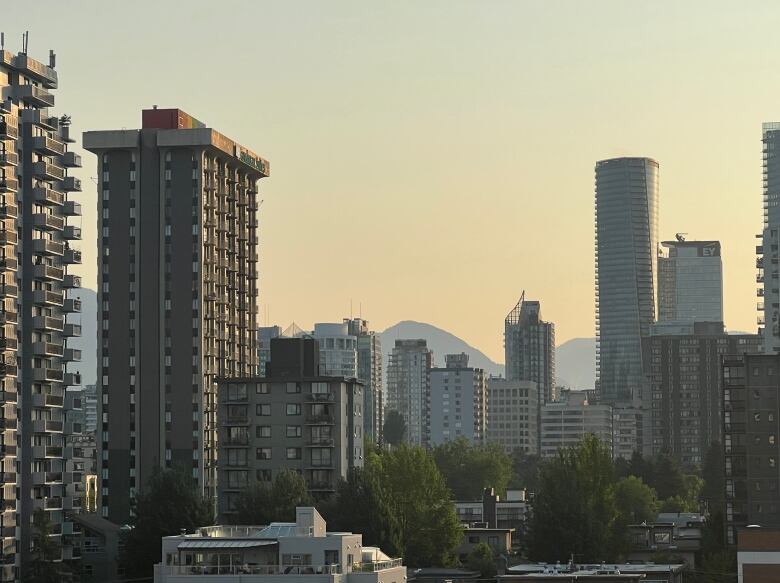 Hazy view from Vancouver's West End neighbourhood, looking toward building towers, against a backdrop of the North Shore Mountains.