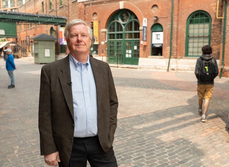 A man stands on brick streets with an industrial brick building behind him.