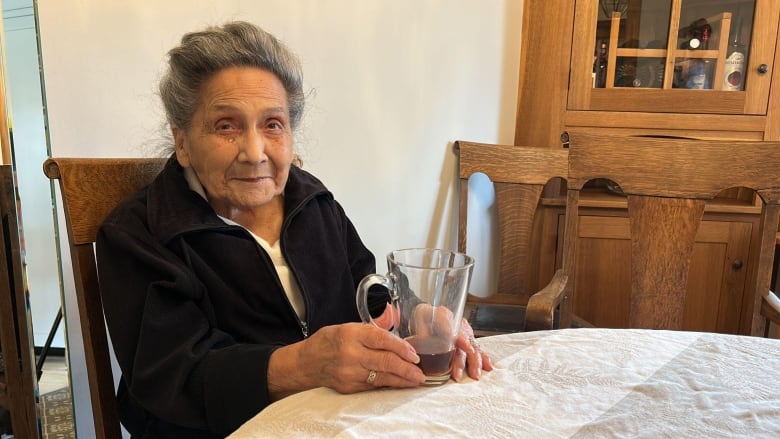 A woman sits at a table holding a mug in her hand.