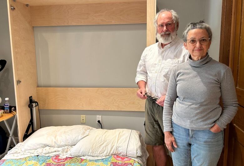 A woman and a man stand next to a Murphy bed that is folded down 