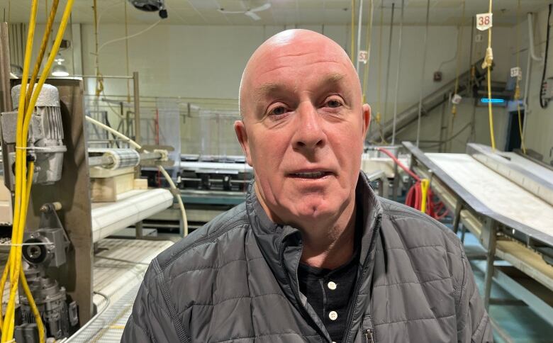 A man in a grey jacket stands inside a processing plant.