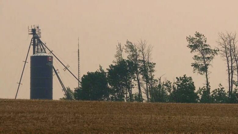 A silo in a field under a light orange sky, presumably from smoke due to wildfires.