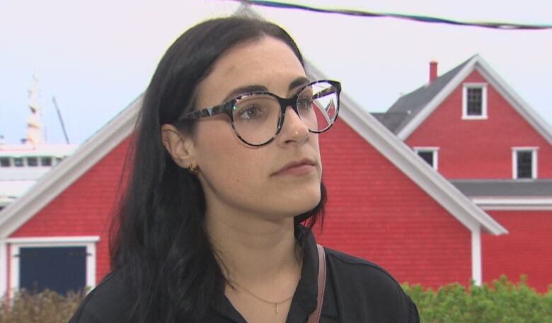 A woman wearing glasses and a black shirt stands in front of red house.