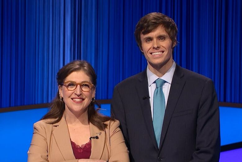 A man and woman smiling. The background is blue with blue curtains. 