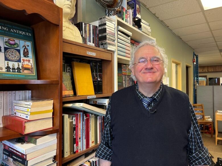 A man smiles in front of a bookshelf