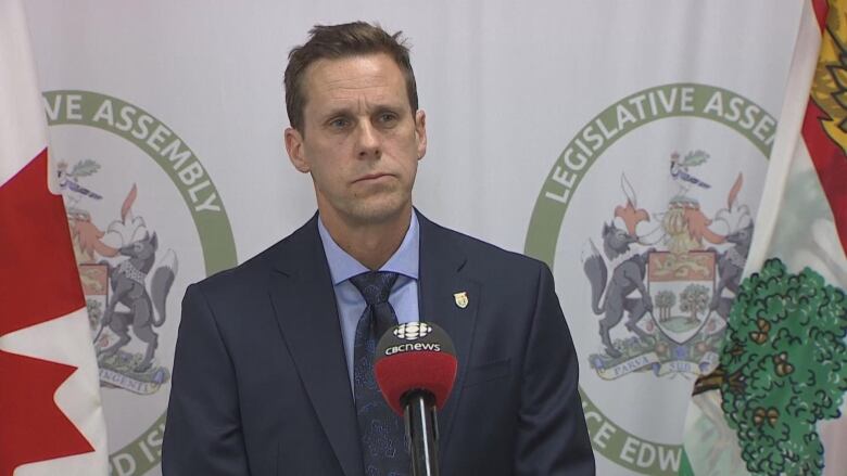 Man in blue blazer stands in front of flags at PEI legislature