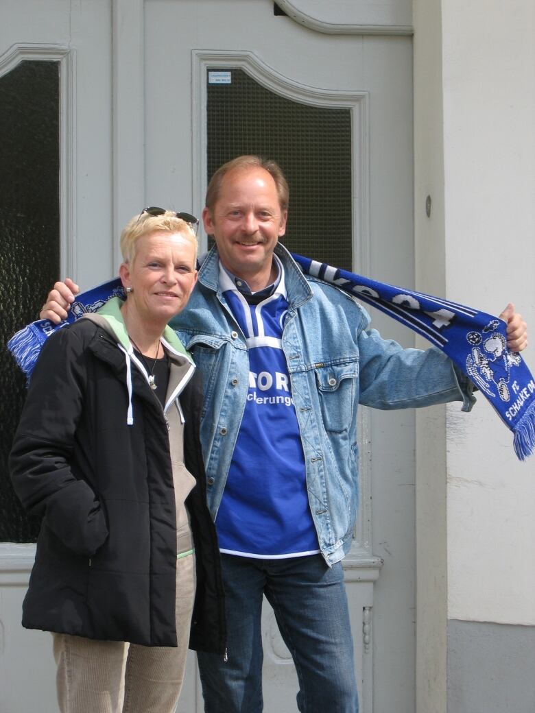 A man and a woman stand in front of a closed door, posing for a picture.