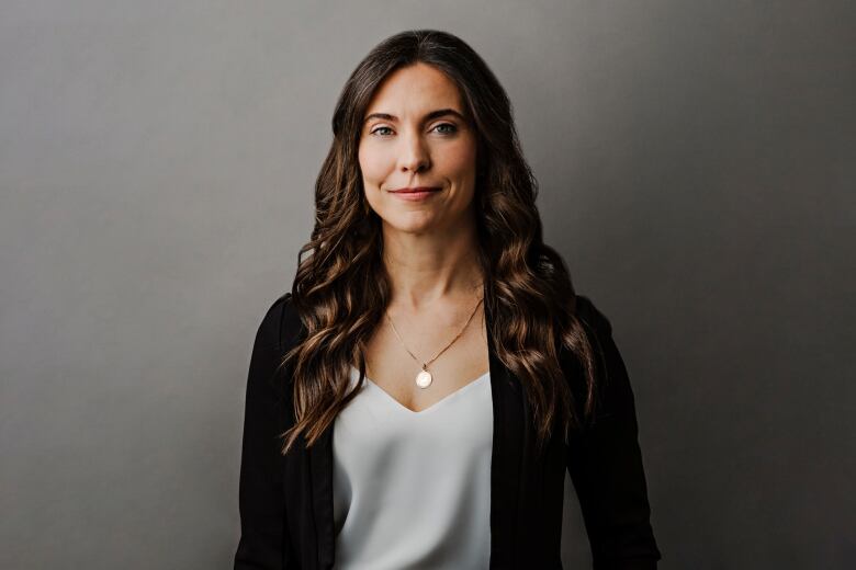 A woman with long brown hair, a black cardigan and a white shirt.