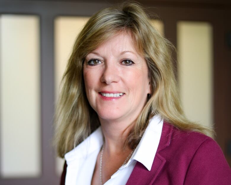 A woman with blond hair wearing a white button-up shirt and a maroon blazer.