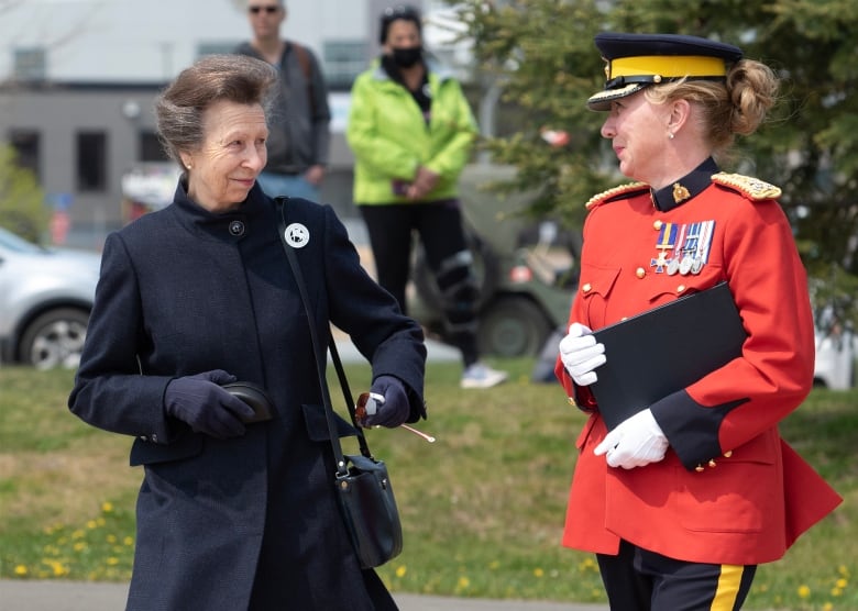 A woman wearing a dark blue coat walks alongside a uniformed member of the Royal Canadian Mounted Police 