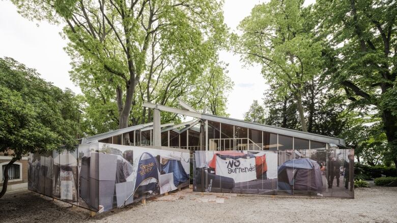 A glass pavilion sitting among trees is partially covered in pictures of tents.